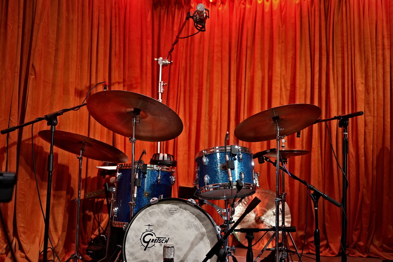The full Gretsch Round Badge kit set up to record, blue sparkle drums against a red curtain